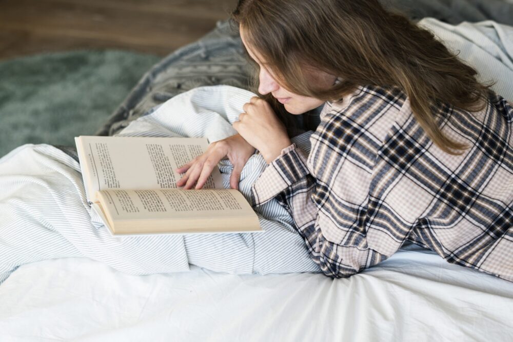 Teen woman reading book in bed